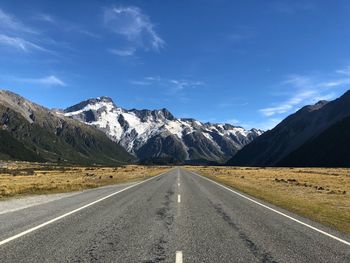 Empty road by mountains against blue sky