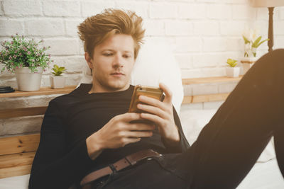 Young man using smart phone while sitting on laptop