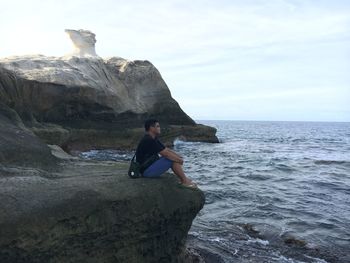 Full length of young man on rock at beach against sky