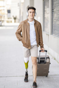 Handsome young man with disability pulling luggage on footpath