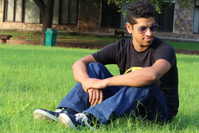 Young man looking away while sitting on grassy field