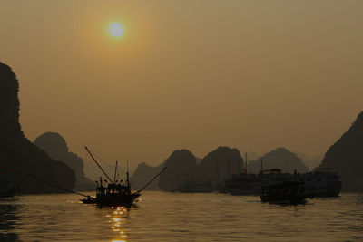 Silhouette boats on halong bay by rock formations against clear sky