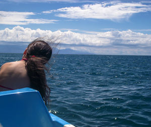 Rear view of woman sitting on boat in sea against cloudy sky
