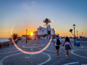 Rear view of people walking on street at sunset