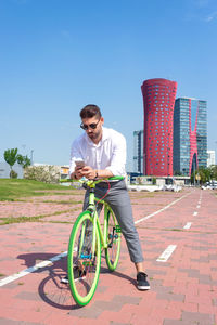 Outdoor portrait of handsome young man with mobile phone and fixed gear bicycle in the street.