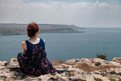 Rear view of woman sitting on cliff against sea