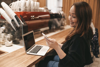 Adult smiling business woman freelancer working in a coffee shop cafe using a laptop and phone