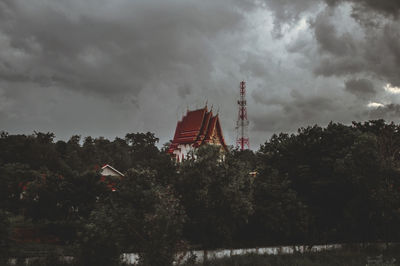 Low angle view of factory by trees against sky