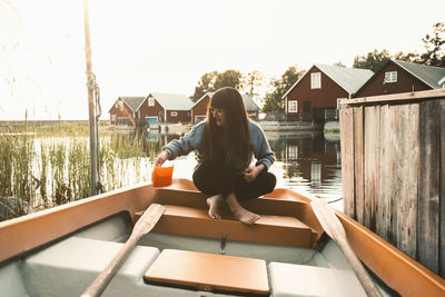 Full length of woman sitting in boat on lake against chalets