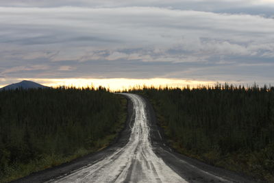 Empty road amidst trees against sky