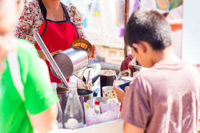 Rear view of mother and son standing by ice cream stall in city