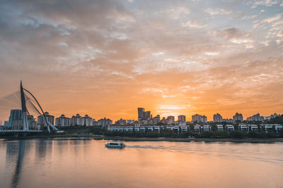 City buildings by river against cloudy sky during sunset