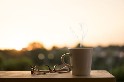 Close-up of coffee cup on table against sky during sunset