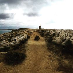 View of lighthouse on rocky beach against cloudy sky