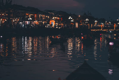 Illuminated city by sea against sky at night