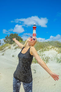 Woman with arms outstretched standing against lighthouse