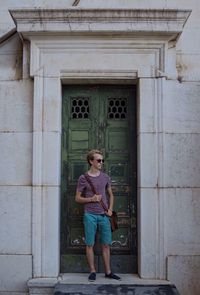 Full length of young man standing by closed green doors