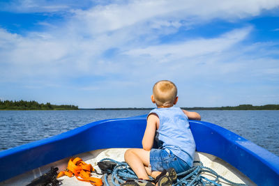 Rear view of boy sitting on boat in lake against sky