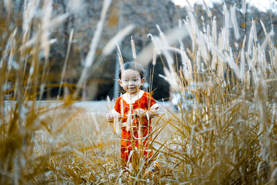 Cute baby boy standing amidst plants on field