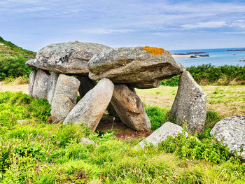 Stack of rocks on field by sea against sky