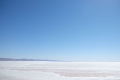 Snow covered landscape against clear blue sky