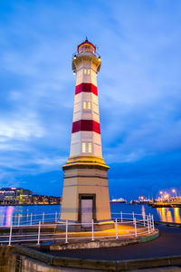 Lighthouse by building against sky at night