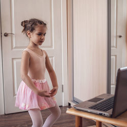 Pretty young ballerina practicing classic choreography during online class, social distance