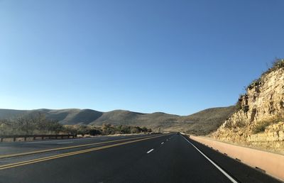 Road leading towards mountains against clear blue sky