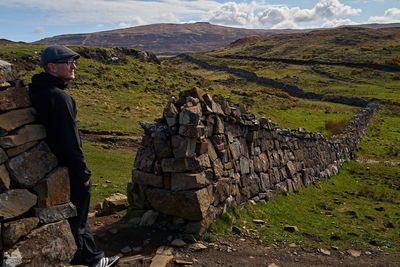 Side view of man leaning on stone wall against mountains and sky