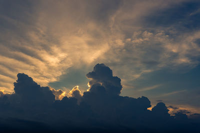 Low angle view of sunlight streaming through clouds during sunset