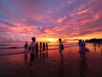 Silhouette people standing on beach against sky during sunset