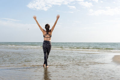 Rear view of a caucasian woman standing in the sea with her arms raised enjoying the sun