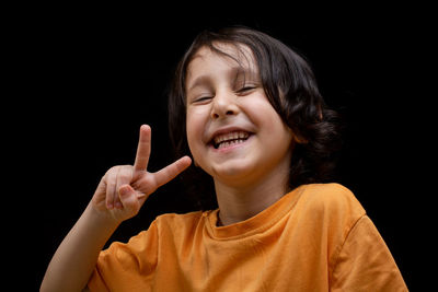 Close-up of cheerful boy gesturing against black background