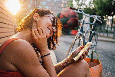 Young woman using mobile phone while sitting in city