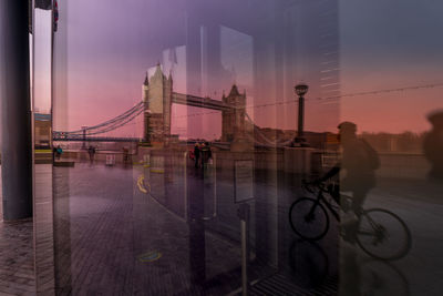 Silhouette people riding bicycle on bridge in city