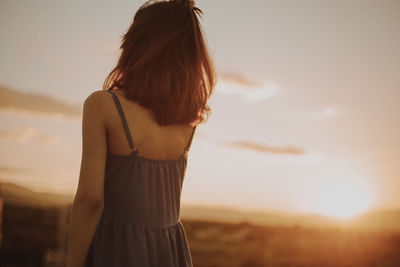 Rear view of young woman standing against sky during sunset