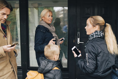 Family standing with mobile phones by house door
