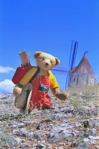 Stuffed toy on field against clear blue sky