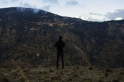 Rear view of man standing on mountain against sky