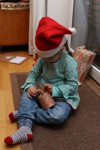 High angle view of cute girl wearing santa hat holding gift while sitting at home