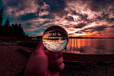 Midsection of person holding crystal ball on beach against sky during sunset