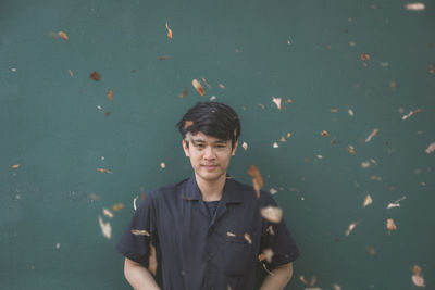 Portrait of young man with blown leaves against wall