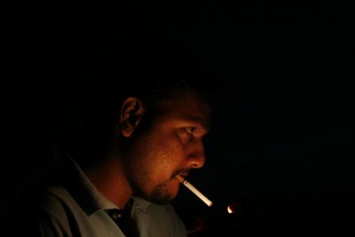 Side view of young man smoking against black background