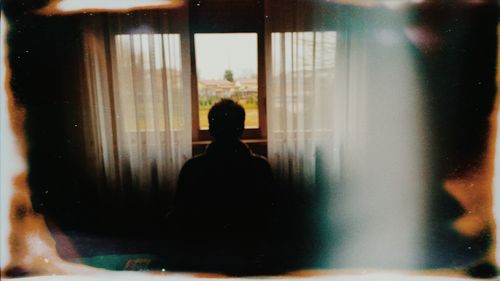 Rear view of silhouette man looking through window