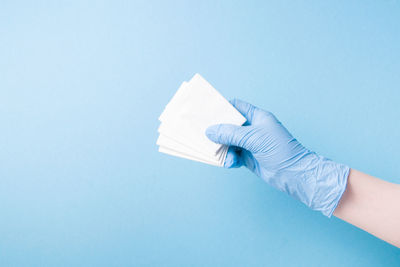 Hand in blue disposable medical glove holds disposable paper napkins