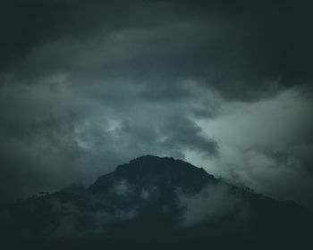 Low angle view of storm clouds over silhouette mountain