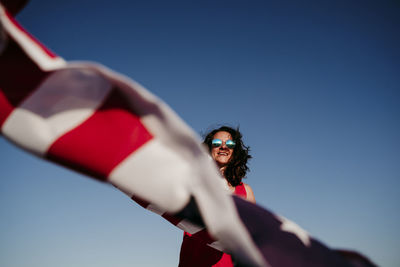 Low angle view of woman holding flag against clear blue sky