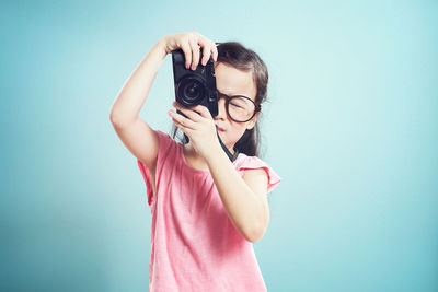 Girl photographing through camera while standing against blue background