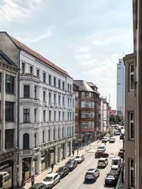 Cars on road by buildings in city against sky