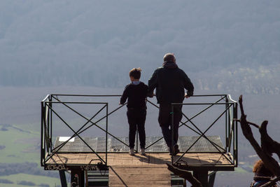 Rear view of people standing on railing against sky